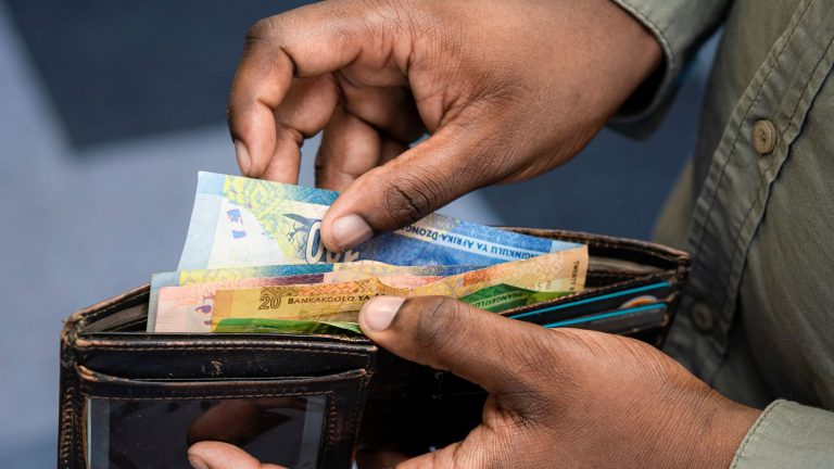 Hands taking South African rand banknotes out of a leather wallet