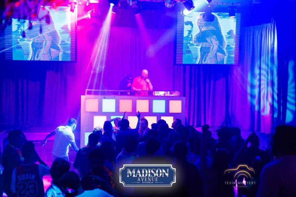 A DJ playing music on stage at Madison Avenue Rivonia with a lively crowd dancing and enjoying the music.
