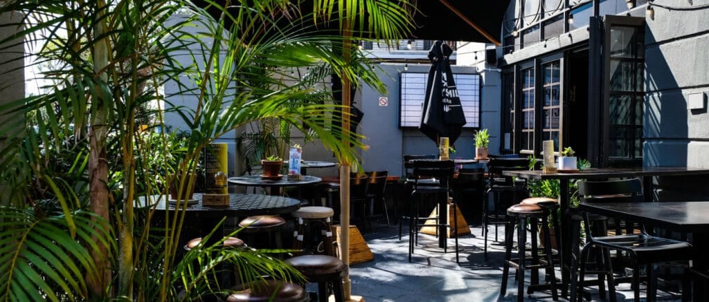 Outdoor seating area at Tiger's Milk bar with tables, chairs, centerpiece plants, and potted plants surrounding the space.