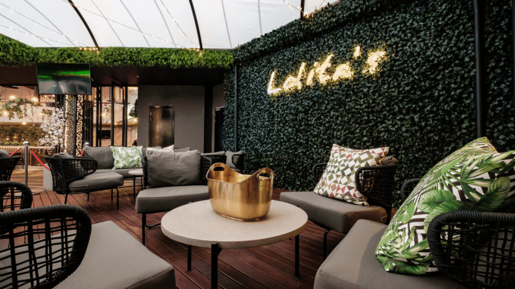 Outdoor patio at Rockets Menlyn with cushy seating, tables, artificial grass walls, and an acrylic roof for weather protection.