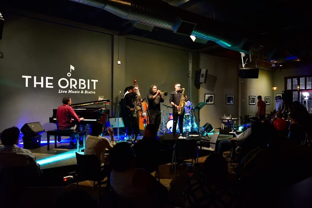 Live band performing on stage at The Orbit in Braamfontein, with an audience seated around enjoying the music.